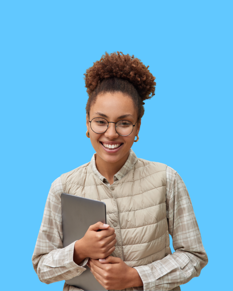 A smiling person with curly hair and glasses wearing a plaid shirt and beige vest, holding a laptop against a solid blue background.