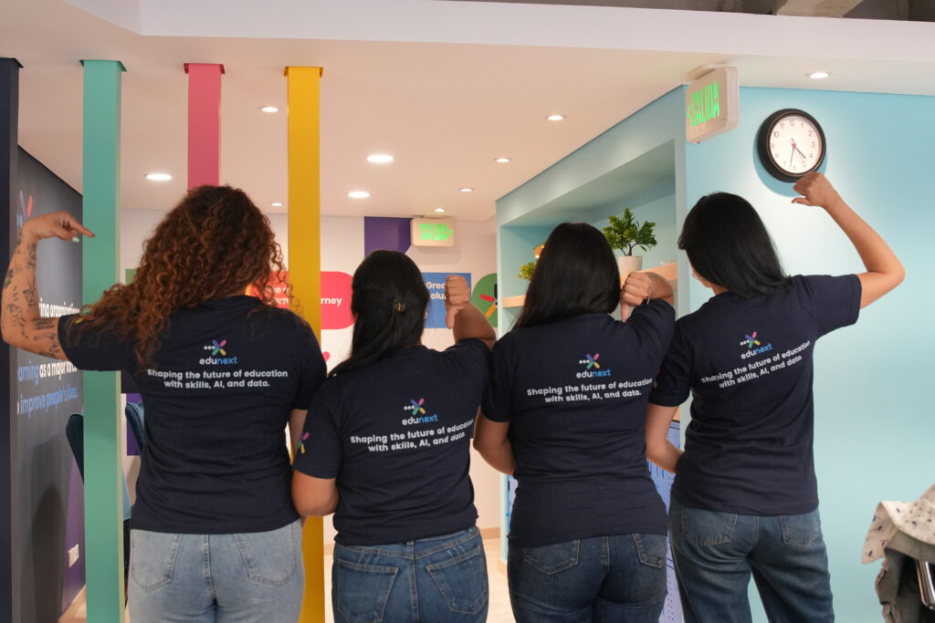 Four people seen from behind wearing navy blue t-shirts with the edunext logo and the text Shaping the future of education with skills, AI, and data.
