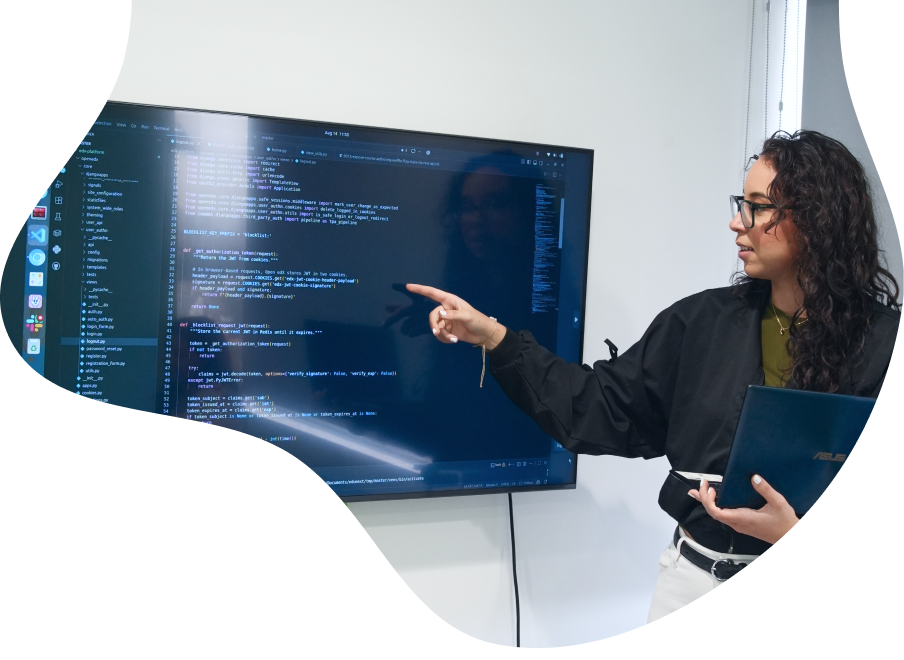 A developer points to a large screen displaying Python code for the Open edX platform while holding a laptop.