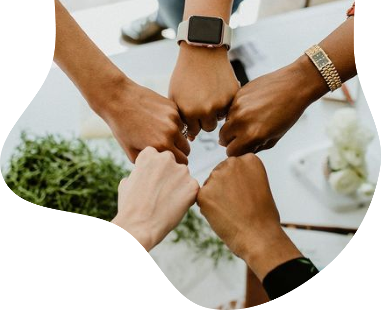 Four people joining their fists together in a collaborative gesture over a desk.