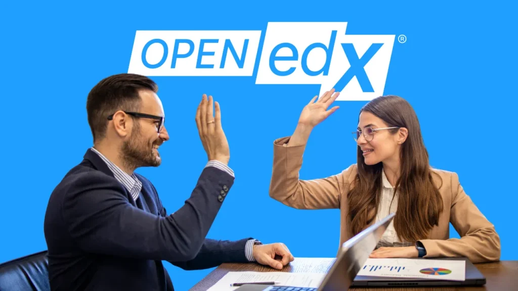 Two professionals sitting at a desk with a laptop and documents, giving each other a high-five in front of an Open edX logo.